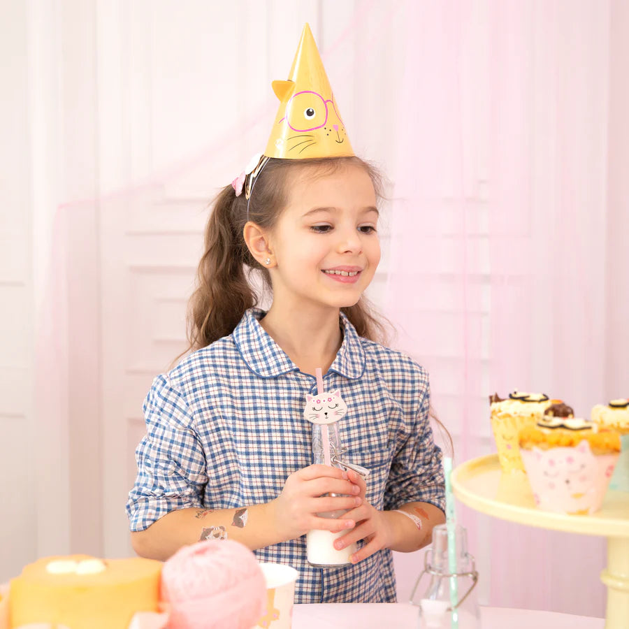Girl wearing a cat-themed party hat, holding a drink with a cat paper straw at a colorful party table.