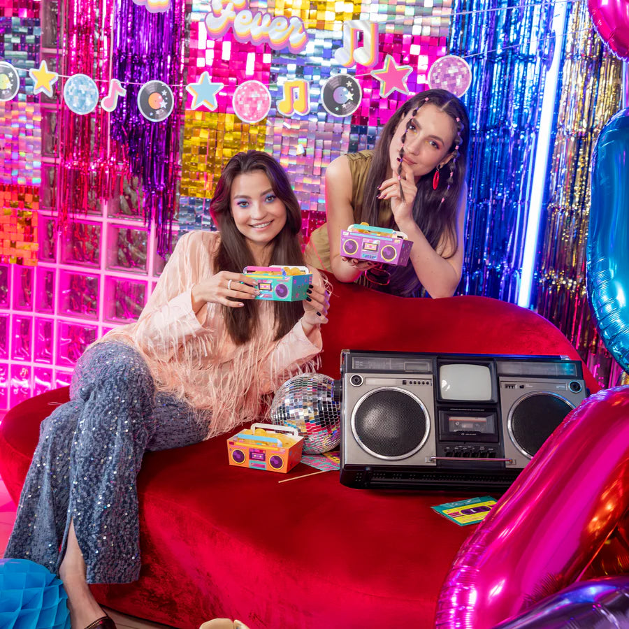 Two women holding colorful retro disco chip boxes in a vibrant party setting with a boombox and disco elements.