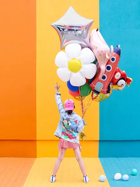 Girl holding colorful foil balloons against a vibrant colored background, celebrating with a peace sign.
