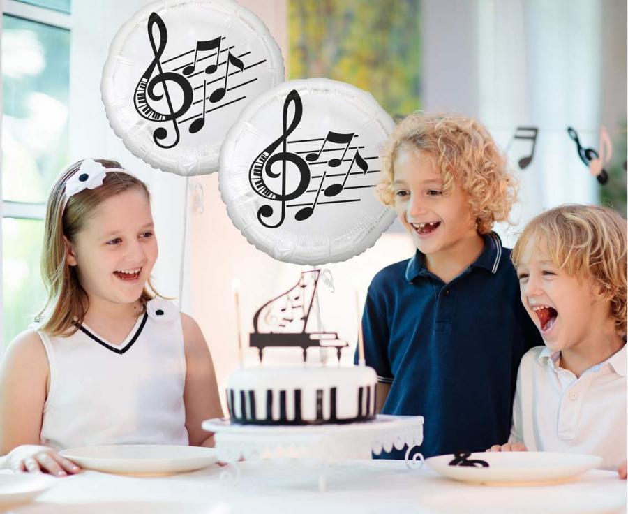 Children celebrating with foil balloon musical notes at a birthday party, featuring a cake and joyful expressions.