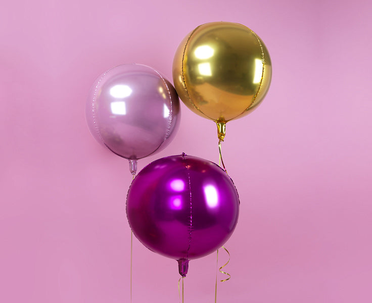 Three foil balloons in purple, pink, and gold colors against a pink background, perfect for celebrations.